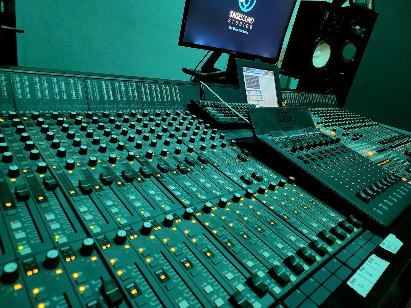 Audio mixing console with illuminated faders and knobs in a studio.